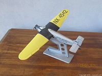 Side view of the model airplane showing the yellow right wing, black text NX 4542, 'Byrd Antarctic Expedition' on the fuselage, mounted on silver stand.