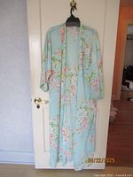 Light blue floral long robe with pink flowers, hanging on a white door.