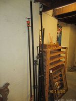 Photo showing multiple long pipe clamps leaning against a basement wall near wooden shelving and framed mirrors.