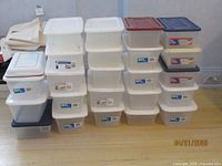 Stack of twenty plus plastic shoe boxes on the floor, various colors and sizes, stacked in 4 uneven columns