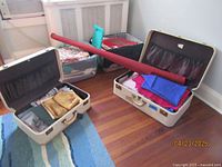 Two white hard suitcases and two clear plastic bins filled with assorted fabrics on hardwood floor