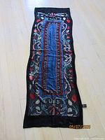 Long rectangular Metropolitan Museum of Art exclusive scarf laid flat showing elaborate colorful geometric and floral design with black border