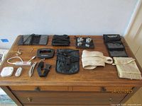 Photo showing an assortment of travel accessories including wallets, luggage scale, power bank, ear buds, neck pouches, money belt, and plug adapters arranged on a wooden dresser.