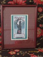Photo of vintage framed advertisement for 'The Merry-Widow' play, showing stylized graphic art with woman in black dress and event details.