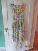 Front view of blue background full apron with yellow roses and floral design hanging on door.