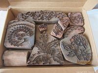 Photo showing assortment of wooden embroidery blocks in various shapes arranged in open cardboard box.