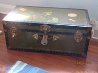 Photo of closed vintage metal travel trunk with decorative travel stickers on the top surface and central lock and clasps visible on front.
