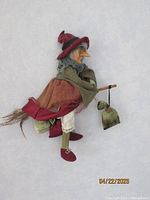 Full side view of the kitchen witch doll showing layered clothing, hat, and sack accessory.