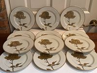 Set of 12 white dessert plates with a gold rose and leaves design arranged for display, showing the front decorations