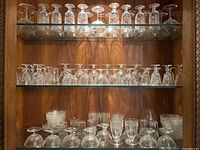 Three wood shelves filled with clear etched stemware and glassware