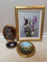 Group shot of four framed floral oil paintings (one rectangular, three oval/round) arranged against wall
