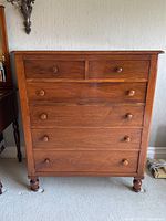 Front view of walnut tallboy chest showing all six drawers and turned bun feet