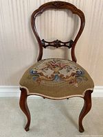Front view showing balloon back wooden frame with carved details and needlepoint floral seat upholstery.
