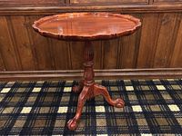 Front view of round wooden side table showing carved pie crust edge and tripod base