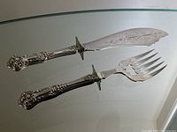 Full view of both fish carving set pieces: knife and fork with ornate sterling silver handles and finely engraved blades.