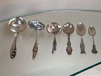 Six spoons and ladles arranged in a row on glass surface