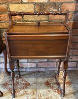 Front view of antique walnut portable sewing cabinet showing rectangular storage box with hinged lid, central turned knob, and turned handle above.