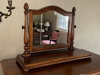 Full view of the antique walnut swing vanity mirror on a wooden surface against a wall with a sconce.