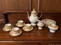 Front view of arranged tea set: teapot, sugar bowl with lid, creamer, 4 cups on saucers.