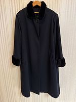 Front view of black wool coat with mink fur collar and cuffs hanging on a hanger