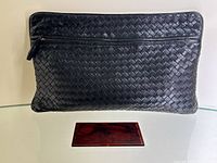 Front view of black woven leather clutch with mirror placed below