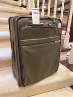 Front view of olive green softside spinner suitcase with front zippered pocket and attached padlock