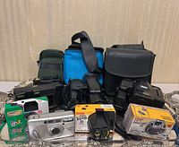 Front view of multiple vintage film cameras, disposable cameras, film rolls, and camera cases arranged on a silver tray.