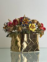 Frontal view of gold plated sterling silver basket with enamel flowers on reflective surface