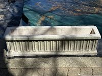 Top-down and front view of rectangular cement garden planter featuring vertical fluted pattern, showing wear and minor chipping consistent with outdoor use.
