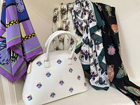 Cream-colored dome handbag with multicolor bug appliqués arranged in front of three hanging scarves