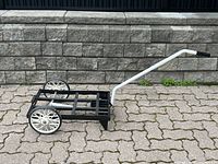 Side view of the two-wheel dolly showing black metal frame, white wheels with spokes, and white handle with black grip.