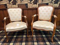 Front view of both carved wood armchairs upholstered in cream fabric with gold wreath pattern