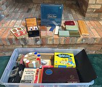 View of multiple board games and decks of cards displayed on brick steps and inside plastic storage bin, includes Scrabble, Yahtzee, score pads, and many card decks.
