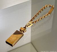 Gold plated perfume bottle charm hanging from linked chain on reflective surface.