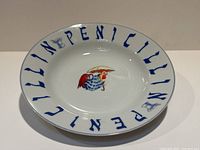 Top-down view of a white ceramic bowl with blue text 'PENICILLIN' around the rim and a red chicken with umbrella illustration in the center.