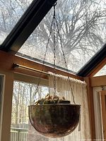 Full view of hanging copper planter suspended near window showing patina and scale