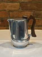 Front side view of the vintage Picquot Ware coffee pot showing the polished stainless steel body and wooden handle.