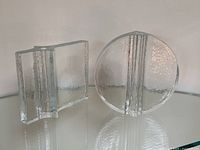 Pair of clear textured solid glass block vases, one round and one rectangular, displayed on a reflective surface.
