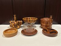 Full frontal view of six wood serving pieces arranged in a line against dark background showing segmented pedestal bowl, cheese dish, condiment holder, and various small bowls.
