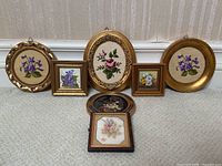 Overview of all seven framed floral artworks arranged on floor against wall