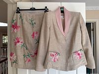 Full front view of jacket and skirt hanging side by side on white backdrop