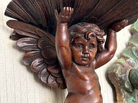 Close-up of cherub figure arms raised holding scalloped shelf