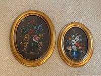 Photo showing both oval framed floral oil paintings side by side on carpet background.