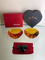 Pair of amber crystal heart-shaped paperweights with original Rosenthal black heart shaped box. Baccarat red box also shown. Green heart brooch with red pouch below the paperweights.