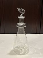 Full view of the clear art glass carafe showing its conical shape and textured neck with the ladybug stopper on top.