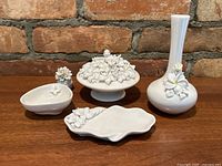 Five porcelain pieces displayed on wooden surface against brick wall