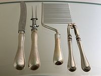 Overview of four utensils on glass surface: carving knife, carving fork, cake cutter, nutcracker