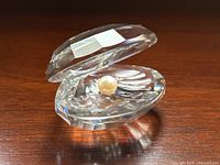 Angle showing facet cuts of clear clam shell crystal and positioned white pearl inside.