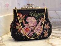 Front view of purse showing floral needlepoint design on black background with gold-tone chain draped