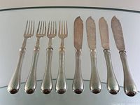 Eight utensils (4 forks, 4 knives) arranged on glass surface